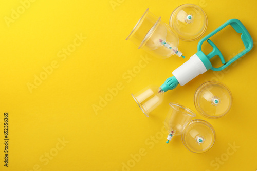 Plastic cups and hand pump on yellow background, flat lay with space for text. Cupping therapy