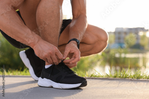 Man tying shoelaces before running outdoors on sunny day  closeup. Space for text