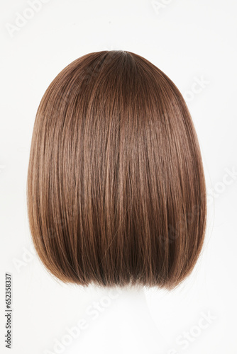 Natural looking dark brunet wig on white mannequin head. Middle length brown hair on the plastic wig holder isolated on white background, back view.
