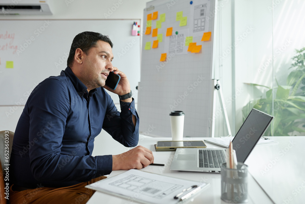 Fototapeta premium Entrepreneur sitting at office desk and talking on phone with client