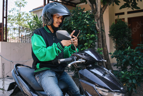 Happy asian man work as a commercial motorcycle taxi driver checking order from his smartphone