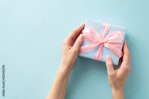 Fototapeta Naklejka Na Ścianę i Meble -  The art of gifting: From first person top view, girl presents a pastel blue gift box adorned with polka dots and a pink ribbon bow, against a pastel blue backdrop for your personal touch