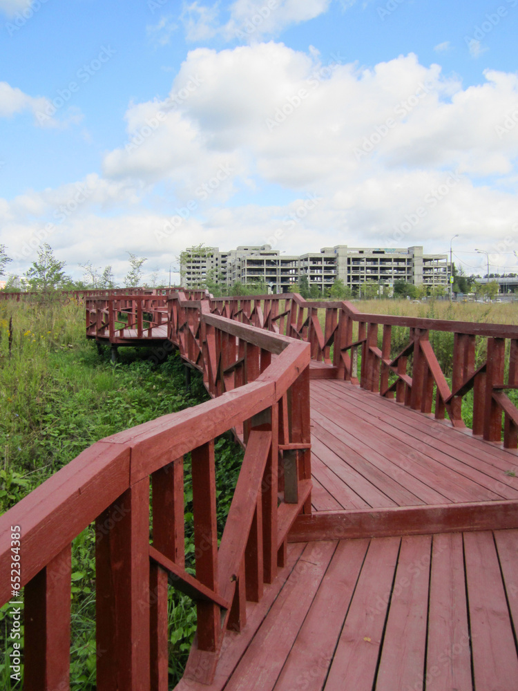 Modern wooden eco-trail with railings against the backdrop of an unfinished building and blue sky.