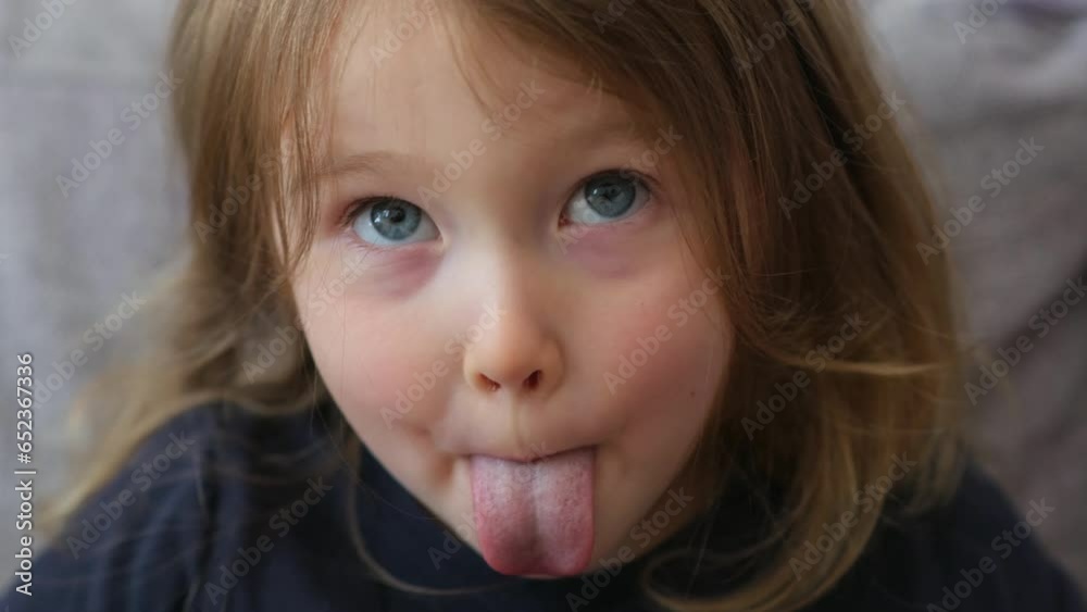 A little beautiful girl sits on the sofa, laughs and plays around. The girl gesticulates and laughs. The facial expressions of a cute child are shot in close-up.