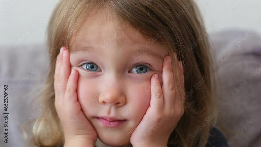 A little beautiful girl sits on the sofa, laughs and plays around. The girl gesticulates and laughs. The facial expressions of a cute child are shot in close-up. A little beautiful girl sits on the sofa, laughs and plays around. The girl gesticulates and laughs. The facial expressions of a cute child are shot in close-up.