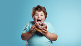 Studio portrait of cheerful fat boy eating a big donut. Concept of child obesity and unhealthy lifestyle, copy space for text