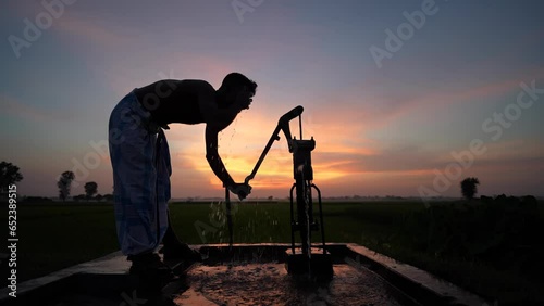 Silhouette of a person using a hand pump, tube well to draw fresh water during a mesmerizing sunset. This evocative video captures the beauty of daily life in rural India.