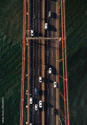 Vertical photo of traffic on bridge crossing the river - top view. Bridge in Lisbon (Portugal) with cars and other vehicles from above (aerial view). Traffic of the road (bridge) on sunset time.
