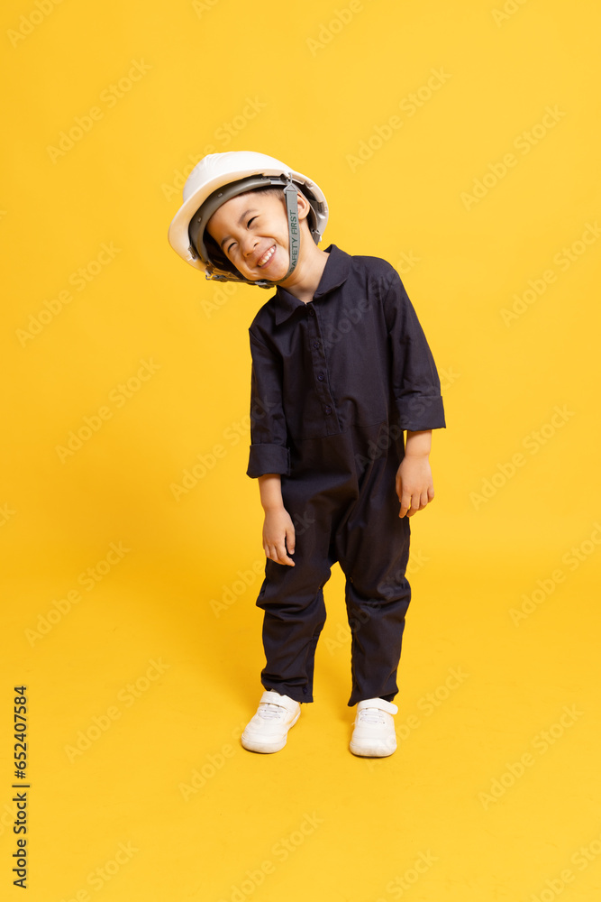 Asian engineer little boy standing and wearing helmet and smiling isolated on yellow background, Technician kid concept Asian engineer little boy standing and wearing helmet and smiling isolated on yellow background, Technician kid concept
