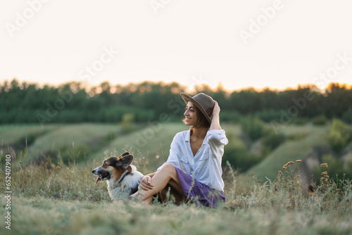 Young lady and her pet Corgi dog spending quality time in nature, overlooking scenic with grassy hills © vitaliymateha