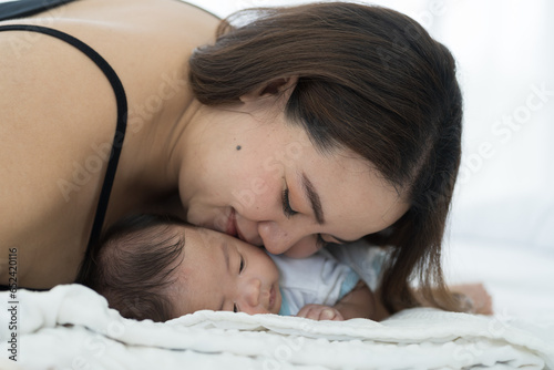 Asian young mother embrancing and kissing newborn baby on white bed. Happy Asian newborn baby and Asian young mother. family, love, happy and new life concept photo