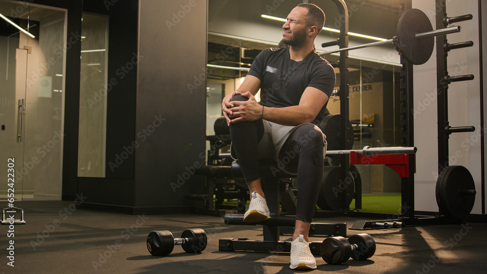 African American unwell man sad suffering with knee pain in sport club ...