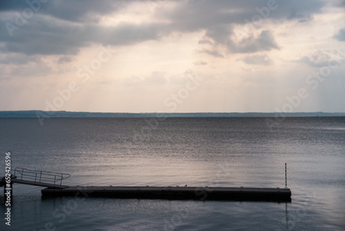 Deserted pier under the rays of the setting sun peering through clouds at dusk