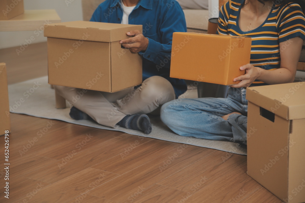 Fototapeta premium Beautiful young couple in love having fun unpacking things from cardboard boxes while moving in together in their new apartment