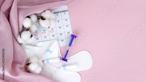 Women's menstrual pads, tampons, female menstruation calendar and alarm clock on a pink background. photo