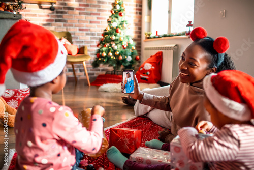 Young African American mother consulting a doctor with her children on a video call on a smartphone during the holidays at home photo