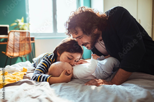 Young Caucasian father and son bonding with a new addition to the family a baby boy in the bedroom at home