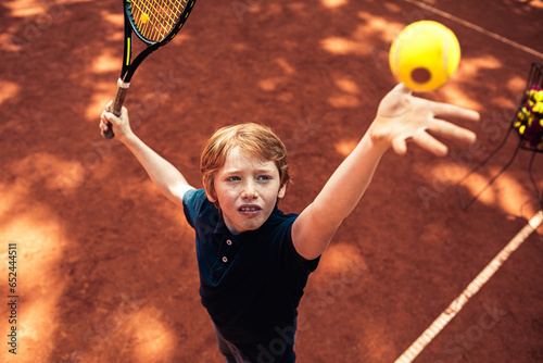 Young Caucasian boy practicing his tennis serve on a outdoor clay court photo