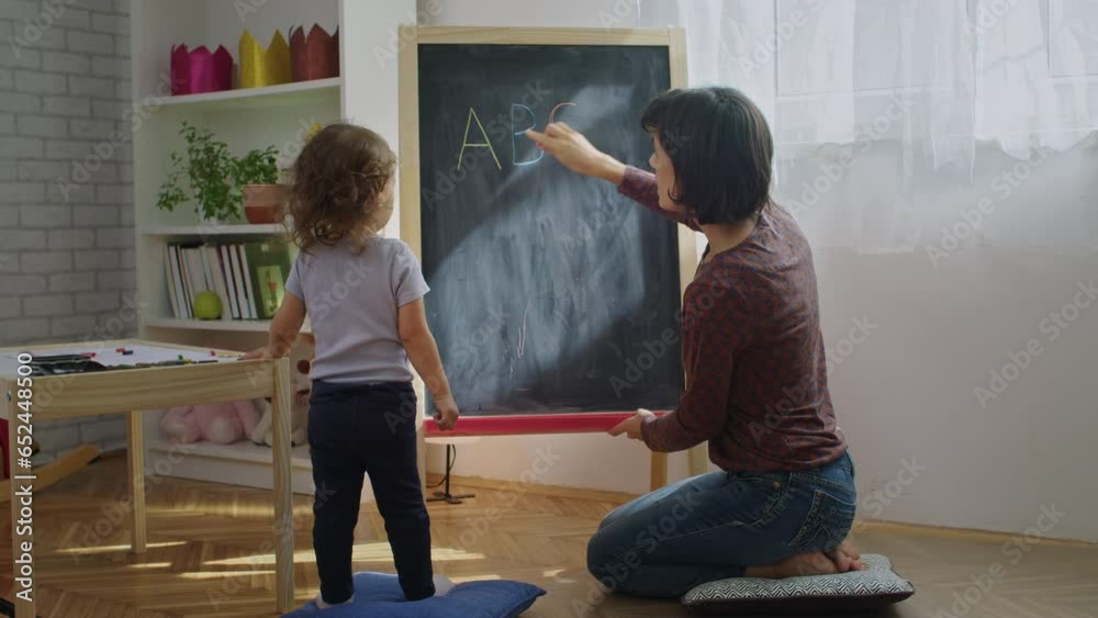 Mother teaching child to write letters on chalkboard at home
