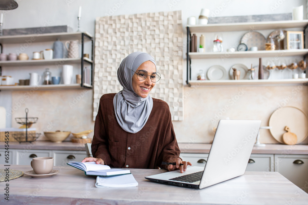 Arab young woman in hijab working remotely at home in the kitchen using ...