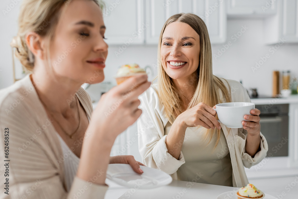 close up two beautiful sisters in casual wear tasting cupcakes and drinking tea, family bonding close up two beautiful sisters in casual wear tasting cupcakes and drinking tea, family bonding