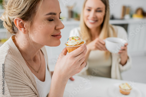 close up two trendy sisters sitting at table drinking tea and eating cupcakes  closed eyes  bonding