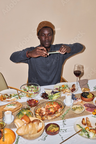 Vertical portrait of young Black man taking photo of Thanksgiving dinner table shot with flash