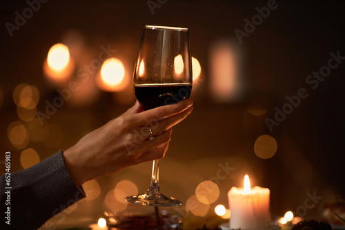 Close up of female hand holding wine glass at dinner table with Christmas lights in background, copy space