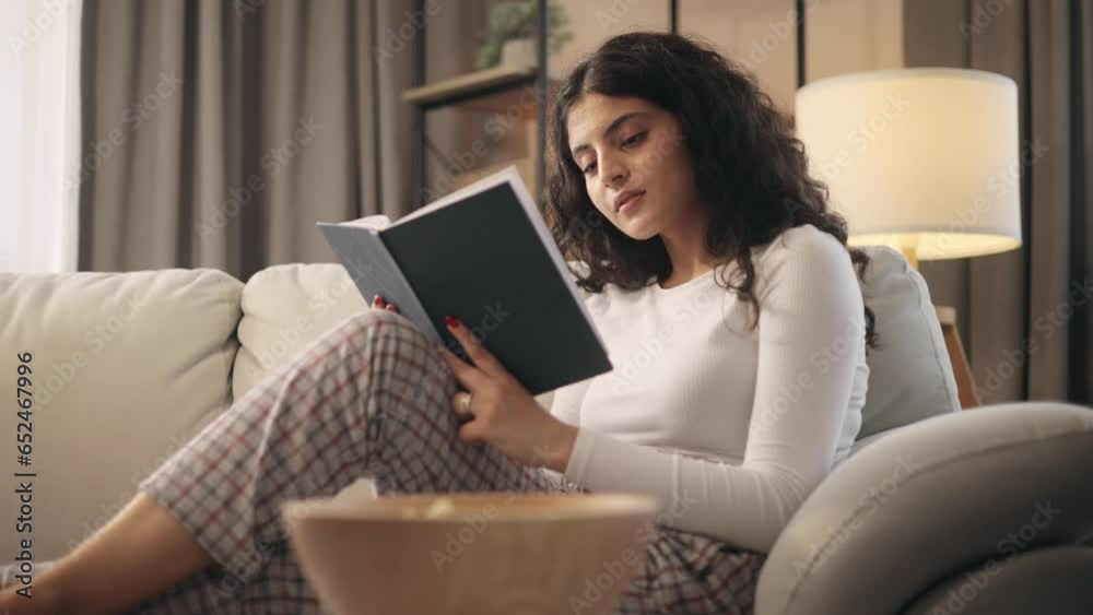 Portrait of charming curly young woman laying on sofa and reading book literature at home Calm relaxed female enjoying weekend leisure time alone indoors. High quality 4k footage Portrait of charming curly young woman laying on sofa and reading book literature at home Calm relaxed female enjoying weekend leisure time alone indoors. High quality 4k footage