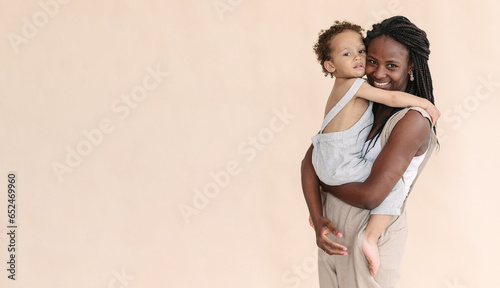 African-American mother with baby smiles and rejoices on beige background Minimalist portraits, space for text