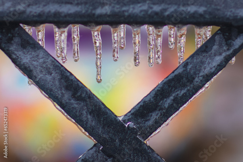 closeup of detail of metal chair covered in dripping icicles against a bokeh colorful background