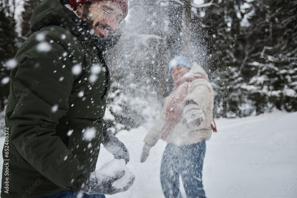 Fototapeta premium Portrait of happy young couple throwing snowballs outdoors in winter and having fun, copy space