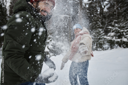 Portrait of happy young couple throwing snowballs outdoors in winter and having fun, copy space