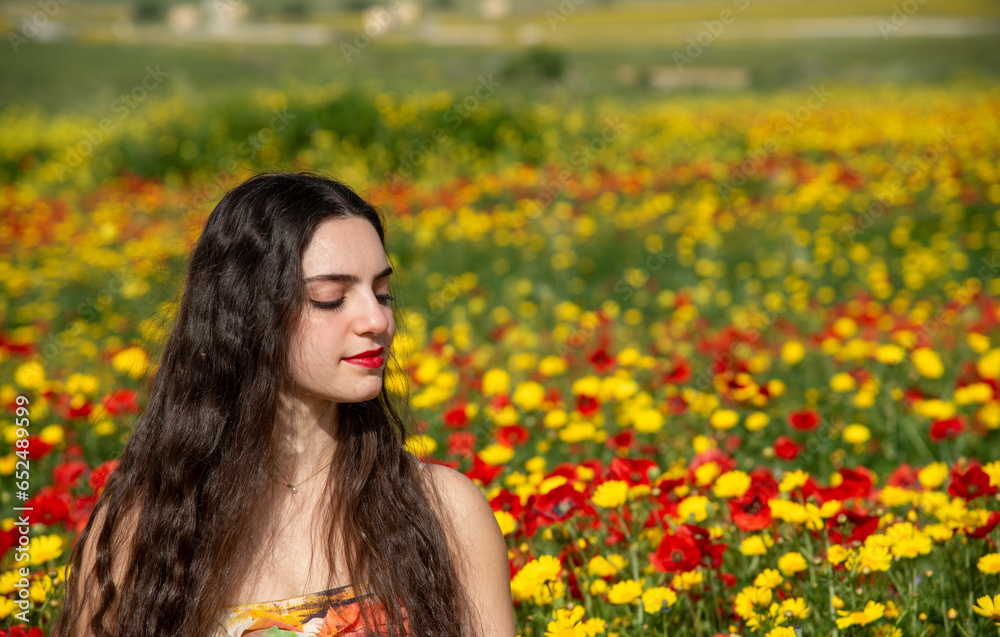 Portrait of a young woman dressed in red smiling in the field of red poppies in spring. Springtime blooming season. Portrait of a young woman dressed in red smiling in the field of red poppies in spring. Springtime blooming season.