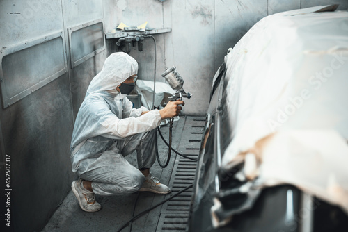 Photography Automotive service worker in full protective gear expertly apply color paint in to car's bodywork with spray gun or respirator painting in chamber workshop