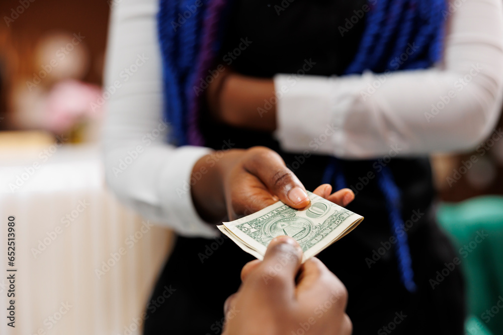 Close up of hotel employee wearing uniform holding money cash taking payment from customer while working in hospitality industry, selective focus. Waitress receiving tip from generous client - obrazy, fototapety, plakaty 
