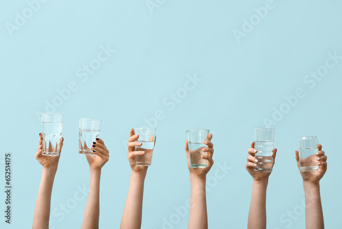 Female hands holding glasses of water on blue background