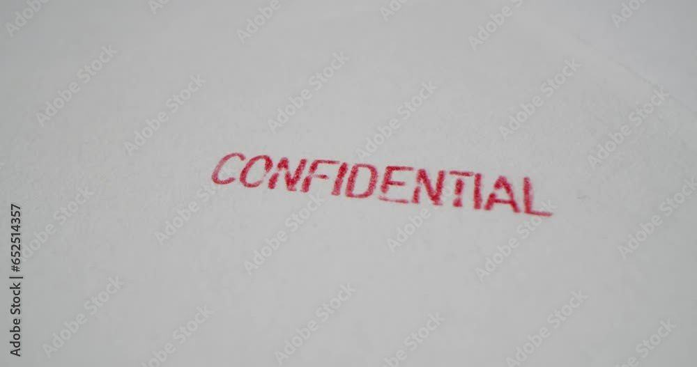 A stamp CONFIDENTIAL is placed on a sheet of white paper, close-up A stamp CONFIDENTIAL is placed on a sheet of white paper, close-up