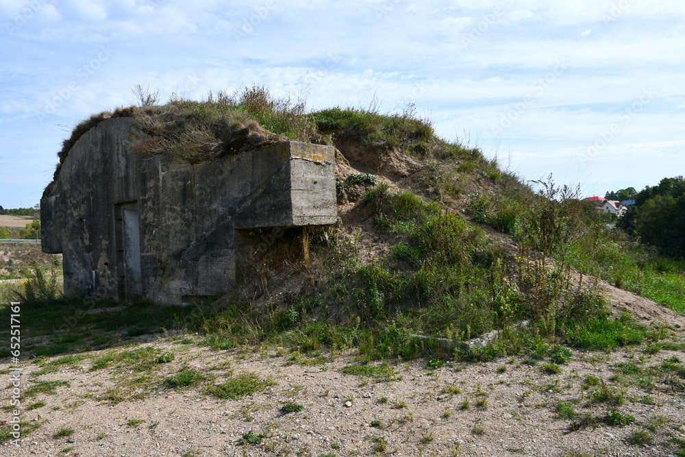 A close up on the remnants of an old concrete bunker or bomb shelter standing on the top of a tall hill next to some road and pavement seen on a sunny summer day on a Polish countryside