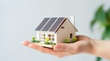A hand holding a model house equipped with solar panels, illustrating the concepts of ecology, sustainability, and energy efficiency, set against a white background