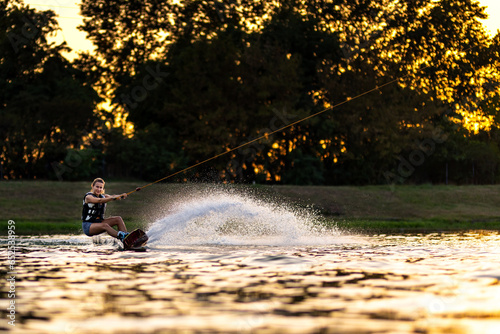 Female wakeboarder wakesurfing on sunset. Girl riding waterski cabel. Holding tow rope. Summer activities in the lake. photo