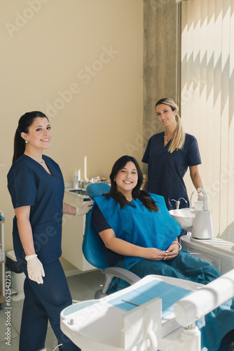 Portrait of three women  dentist  assistant and patient in a dental office smiling and looking at camera.