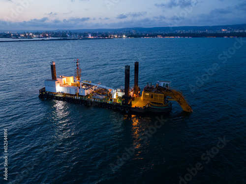 Canvas-taulu Aerial view of a dredge vessel with a dredging bucket, actively deepening the navigational fairway at sea, ensuring safe navigation