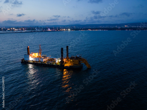 Canvas-taulu Aerial view of a dredge vessel with a dredging bucket, actively deepening the navigational fairway at sea, ensuring safe navigation