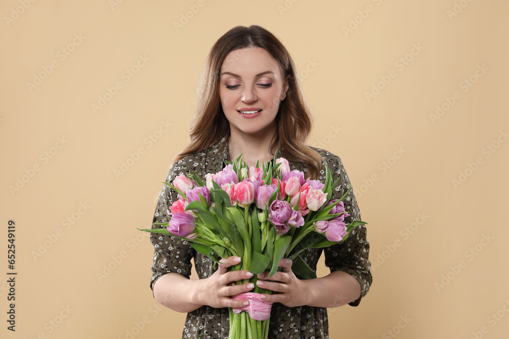 Happy young woman holding bouquet of beautiful tulips on beige background
