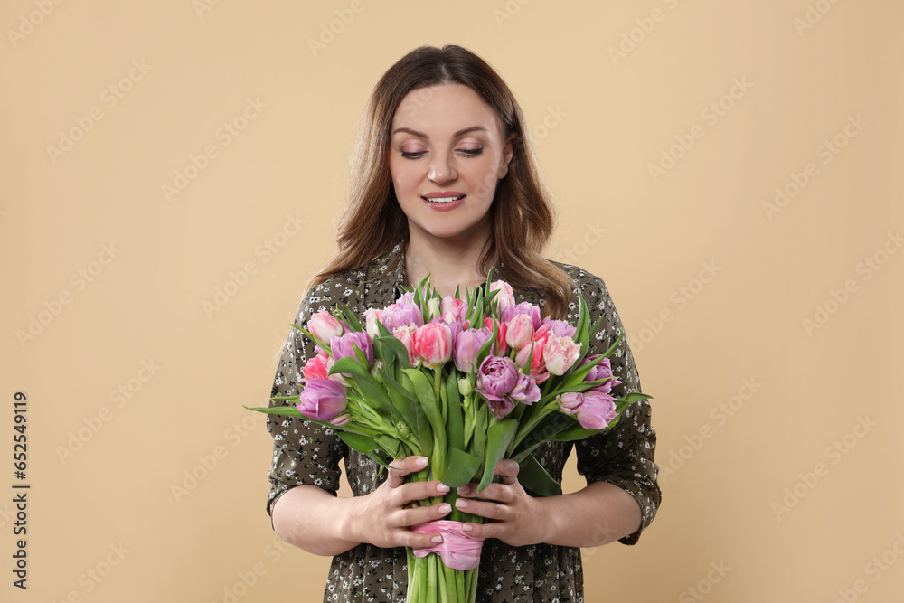 Happy young woman holding bouquet of beautiful tulips on beige background Happy young woman holding bouquet of beautiful tulips on beige background