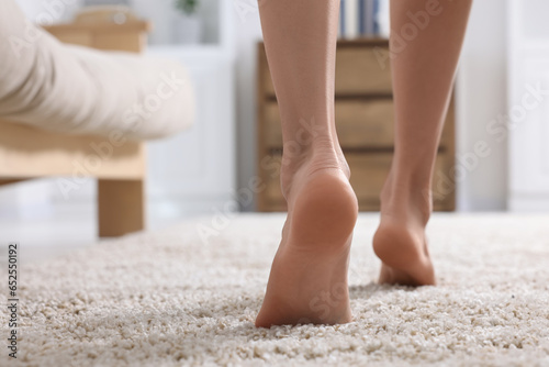 Woman walking on soft light brown carpet at home, closeup. Space for text