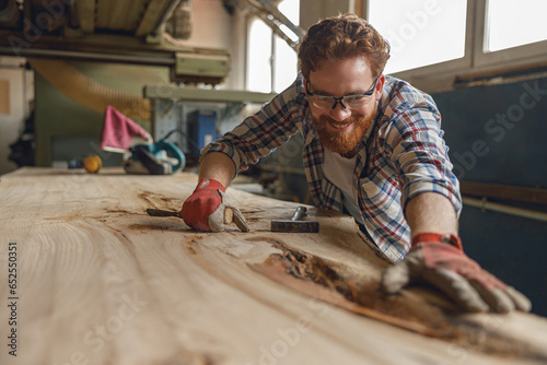 Close up of smiling craftsman working with chisel while cutting wooden plank in carpentry workshop