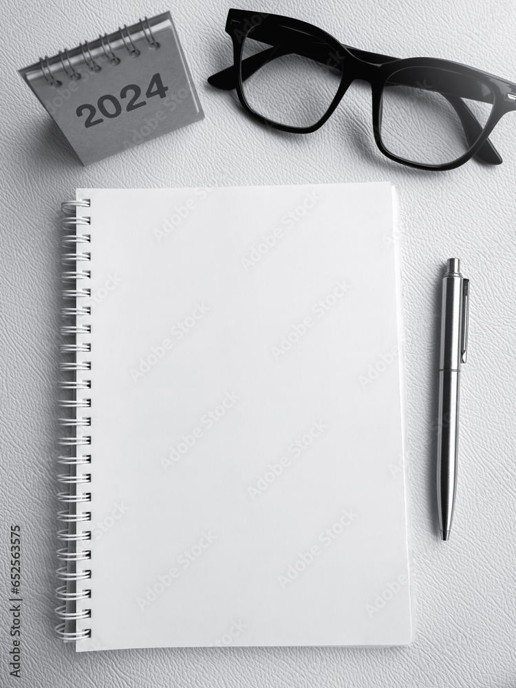 White blank template on notepad with 2024 desk calendar, pen and glasses. Blank paper for draw, sketch, note, to do list, creative and idea concepts. Mockup space vertical page on spiral notebook. White blank template on notepad with 2024 desk calendar, pen and glasses. Blank paper for draw, sketch, note, to do list, creative and idea concepts. Mockup space vertical page on spiral notebook.