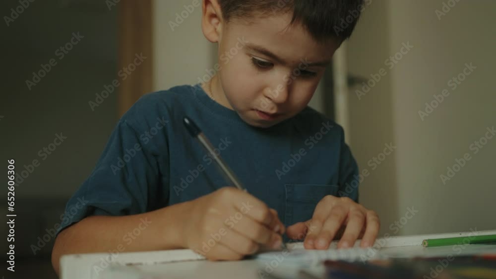 Kid boy studying at home with book, writing in notepad and doing school ...